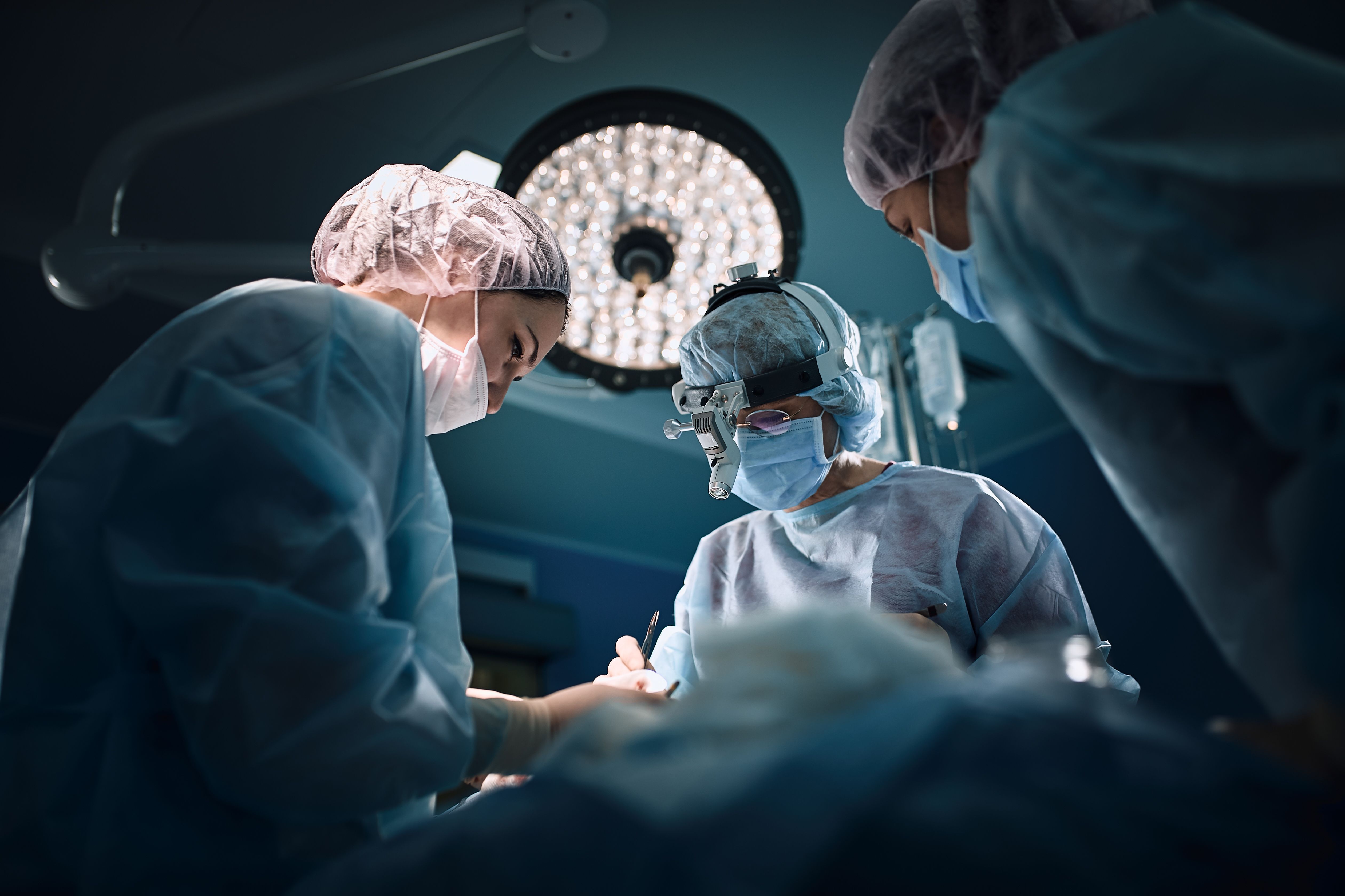 Illustrative photo of three surgeons in an operating room seen from a patient's point of view.